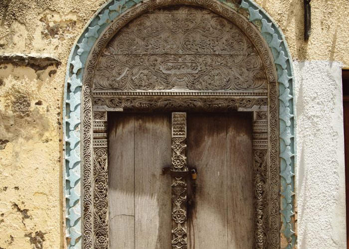 Ornate wooden door in a historical building with intricate carvings and textured facade.